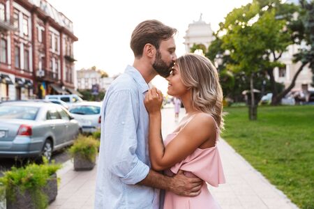 Photo of happy positive cute young loving couple walking by street outdoors looking at each other.の写真素材