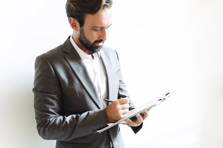 Image of thinking concentrated businessman wearing formal suit reading documents and writing down...