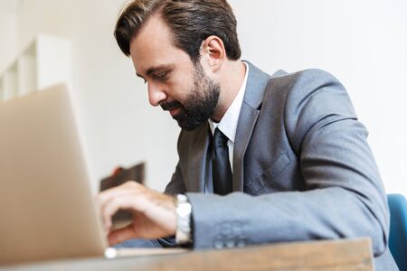 Photo of a handsome concentrated bearded business man sitting in office using laptop computer working indoors.の写真素材