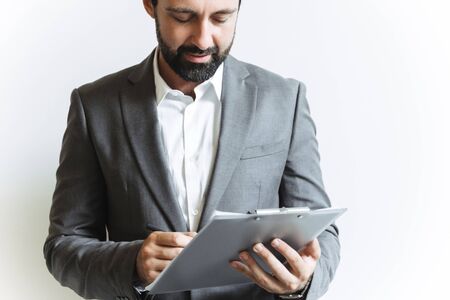 Image closeup of handsome successful businessman wearing formal suit holding clipboard and writing down notes while working in officeの写真素材