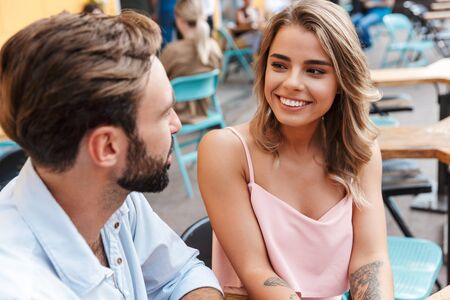 Image of smiling happy cheerful cute young loving couple outdoors sit in cafe talking with each other.の写真素材