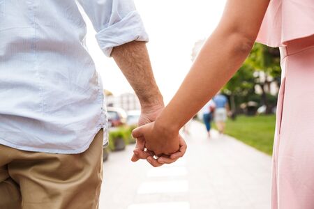 Cropped photo of a young loving couple walking by street outdoors holding hands of each other.の写真素材