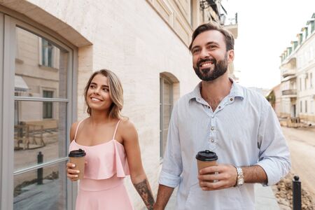 Photo of positive optimistic cheery cute young loving couple outdoors walking drinking coffee.の写真素材
