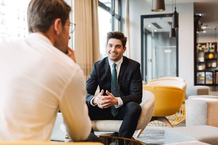 Image of a cheery smiling businessmen colleagues indoors in business center office talking with each other.の写真素材
