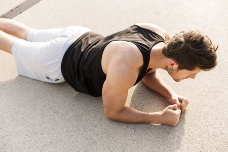 Photo of muscular man in sportswear working out on floor at green park outdoors in morningの写真素材