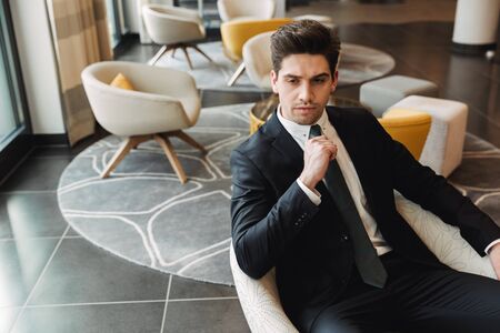 Photo of a young serious businessman indoors in business center office.