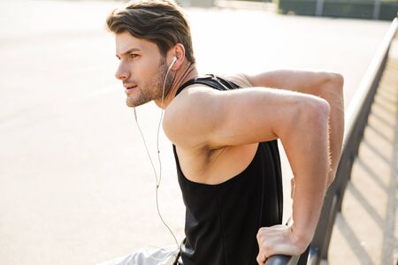 Photo of runner man in sportswear wearing earphones standing on sports ground during morning workout outdoorsの写真素材