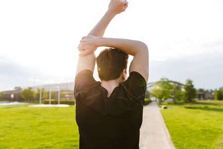 Image of young man in sportswear working out and running at green park outdoors in morning