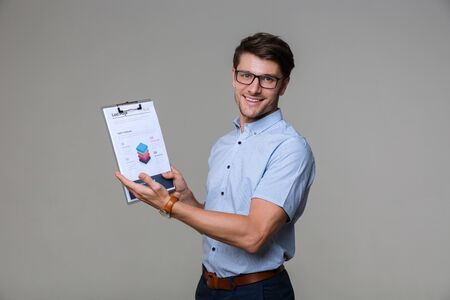 Image of a cheery pleased business man posing isolated over grey wall background showing clipboard.の写真素材
