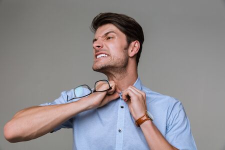 Image of emotional business man isolated over grey wall background try to take off his shirt holding...