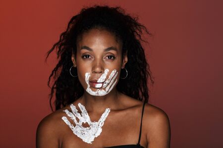 Image of a serious african young woman isolated over red wall background with hand print on face and clavicles.の写真素材
