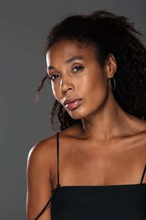 Portrait of an attractive young african woman with long curly hair posing while standing isolated over gray background, looking at cameraの写真素材