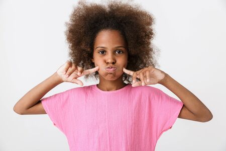Cheerful funny little african girl wearing pink blouse standing isolated over white background, grimacingの写真素材