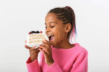 Image of happy african american girl holding and eating piece of torte isolated over white backgroundの写真素材