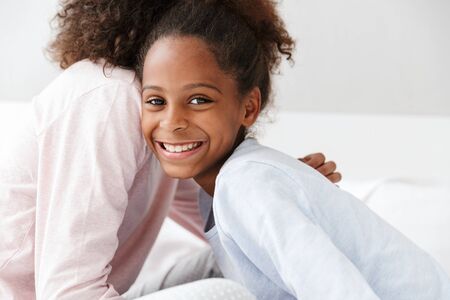 Image of joyful african american woman and her little daughter smiling and sitting on sofa at homeの写真素材