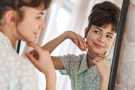 Image of a young happy cheery beautiful woman indoors at home looking at mirror.の写真素材