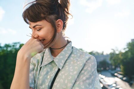 Photo of a cute shy young beautiful woman photographer with camera on a balcony.の写真素材