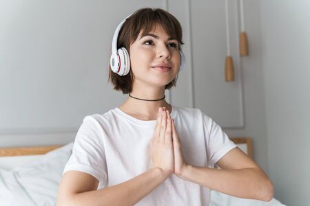 Photo of a pleased concentrated beautiful young lady indoors at home listening music with headphones meditate looking aside.の写真素材