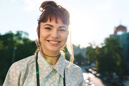 Photo of a positive pleased happy young beautiful woman photographer with camera on a balcony.の写真素材