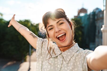 Photo of a young cheerful emotional optimistic pretty woman on a balcony take a selfie by camera.の写真素材