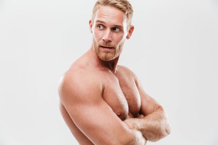 Handsome young concentrated shirtless sportsman standing with arms folded, looking away isolated over white backgroundの写真素材