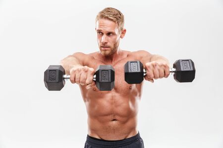 Confident attractive young muscular shirtless sportsman standing isolated over white background, lifting heavy barbellsの写真素材