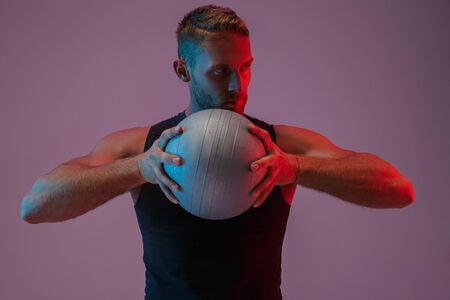 Image of a handsome concentrated young sports man posing isolated over neon lights holding ball.の写真素材