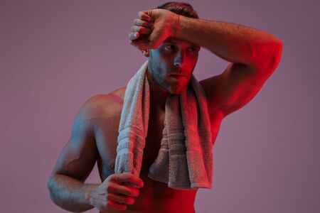 Portrait of handsome serious strong young sports man posing isolated over neon lights with towel.の写真素材
