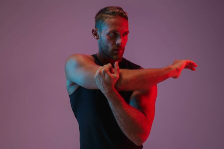 Portrait of a handsome fit muscular sportsman standing isolated over background, doing stretchingの写真素材