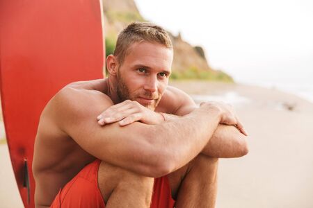 Image of a positive strong handsome man surfer with surfing on a beach outside.の写真素材