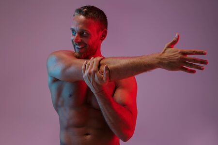 Portrait of a handsome fit muscular shirtless sportsman standing isolated over background, doing stretchingの写真素材