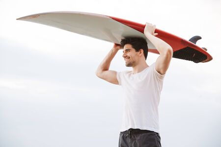Photo of a positive happy handsome man surfer with surfing on a beach outside.の写真素材