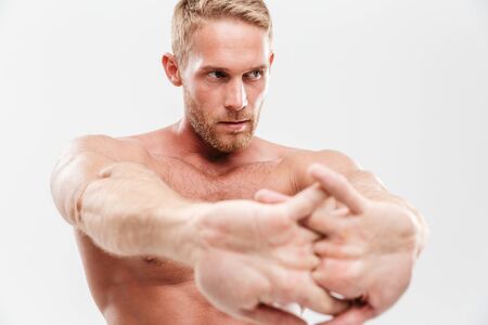 Handsome young concentrated shirtless sportsman doing stretching exercises while standing isolated over white backgroundの写真素材