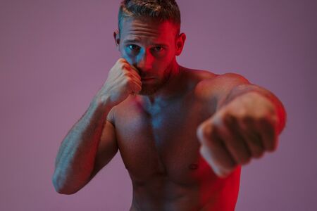 Image of a handsome strong young sports man posing isolated over neon lights boxing.