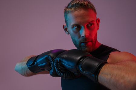 Image of a serious strong young sports man boxer posing isolated over neon lights in gloves.の写真素材