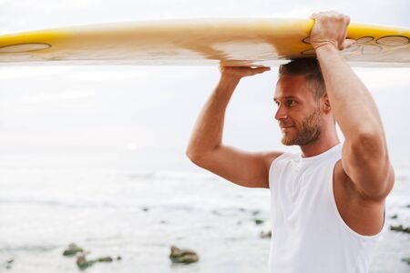 Photo of a positive optimistic handsome man surfer with surfing on a beach outside.の写真素材