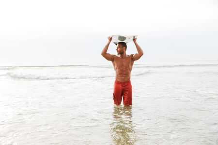 Image of a serious strong handsome man surfer with surfing on a beach outside.の写真素材