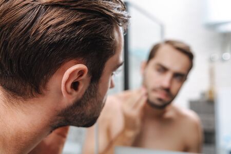 Concerned young shirtless man looking at himself at the bathroom mirrorの写真素材