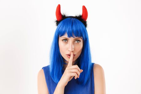 Portrait of young nice woman wearing blue wig and toy devil horns gesturing silence sign isolated...