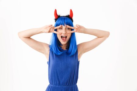 Portrait of cute funny woman wearing blue wig and toy devil horns gesturing peace sign while winking isolated over white backgroundの写真素材