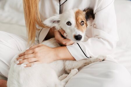 Cropped closeup photo of a young cute girl in pajama at home on bed with her dog cuddling.の写真素材