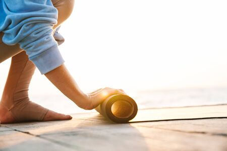 Cropped photo of young fitness woman outdoors on beach with fitness rug.の写真素材