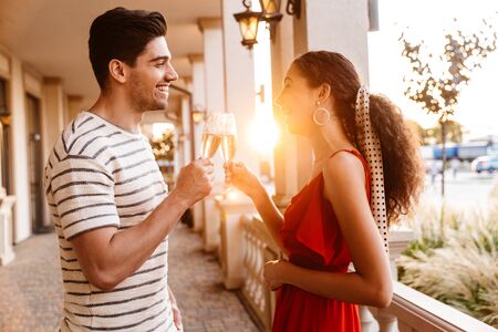 Image of happy caucasian couple laughing and drinking champagne while standing near beautiful buildingの写真素材