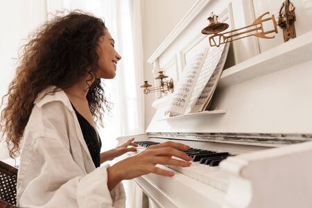 Photo of a beautiful smiling young lady in lingerie and white shirt play the piano indoors at home.の写真素材