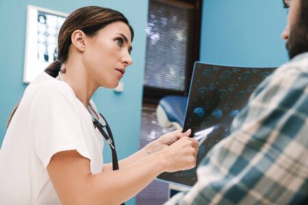 Image of female doctor in medical uniform and young patient man looking at x-ray scan computed...