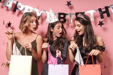 Image of glamour party girls in fancy dresses unpacking birthday gifts isolated over pink backgroundの写真素材