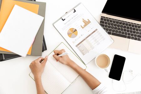 Top view of a businesswoman taking notes in notebook over office desk