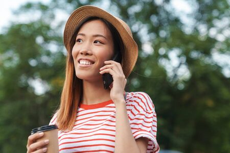 Image of a young happy cheerful beautiful asian woman walking outdoors talking by mobile phone.の写真素材