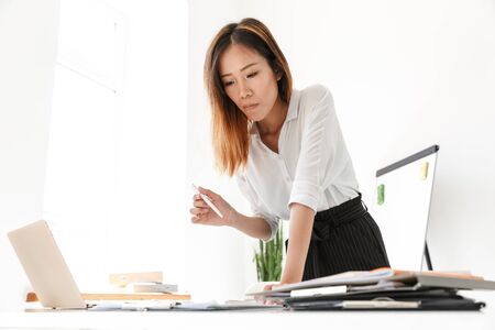 Beautiful young asian businesswoman standing at her desk in office, working on laptop computerの写真素材