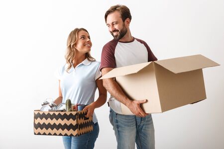 Photo of pleased couple in casual clothing holding cardboard boxes while looking at each other...